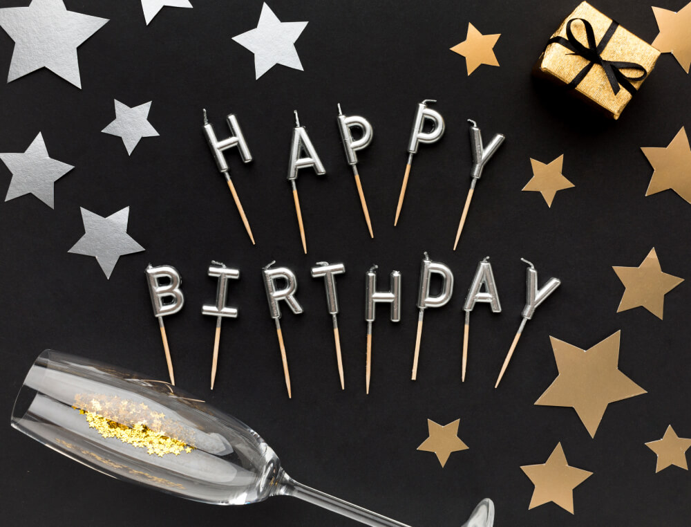 Stilvolle Happy-Birthday-Deko mit goldenen Sternen und Sektglas auf dunklem Hintergrund